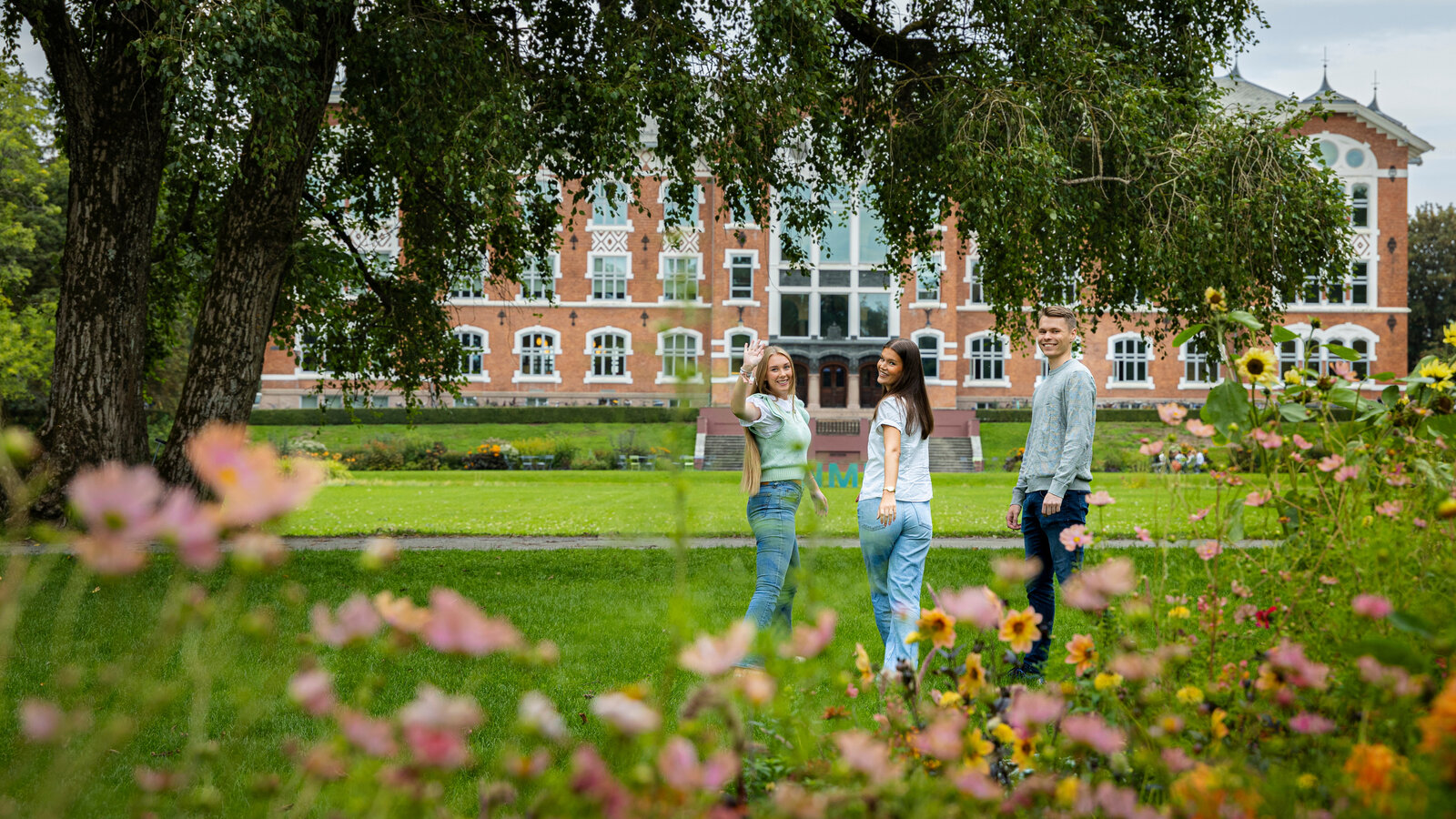 studenter står på en plen foran en mursteinsbygning og vinker