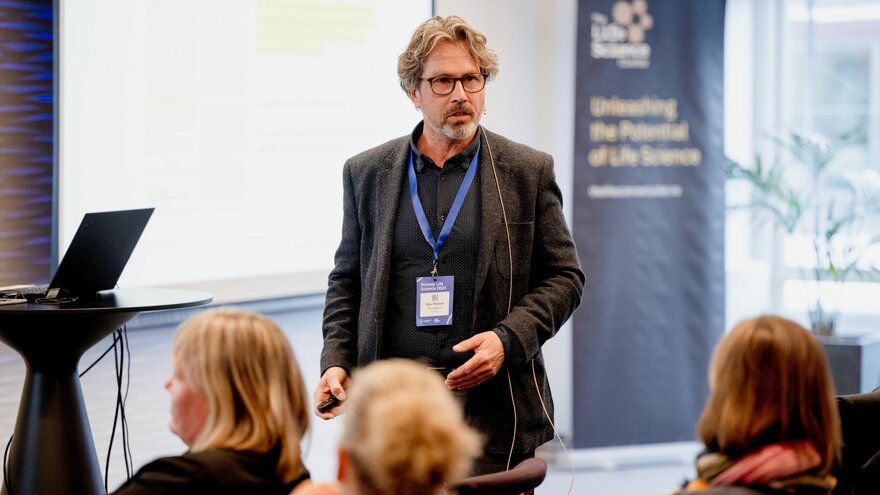 Professor Olav Reksen innledet på Livsvitenskapskonferanse 2024. Tavle og banner i bakgrunnen.