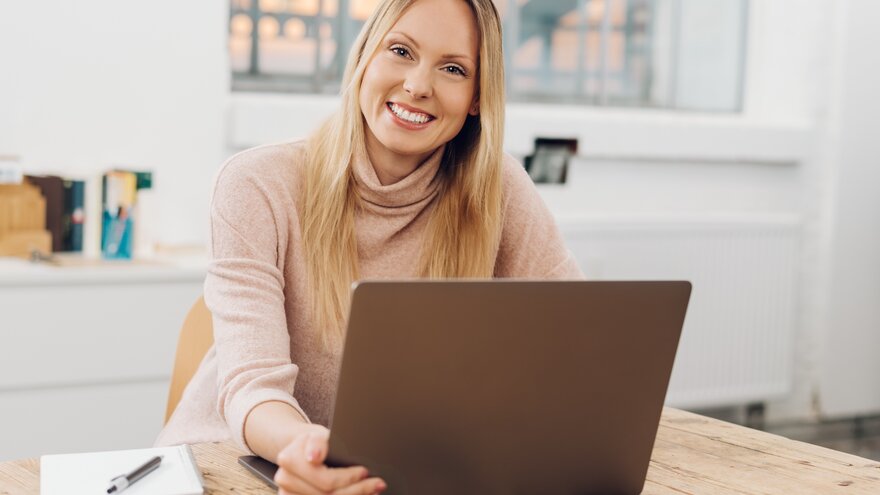 Kvinne som smiler til kamera mens hun sitter ved PC.