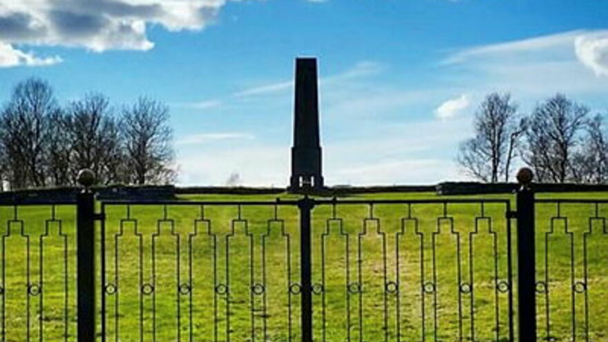 Photo from Tjøtta 2009: A metal fence on a green field, tower and sky in the background