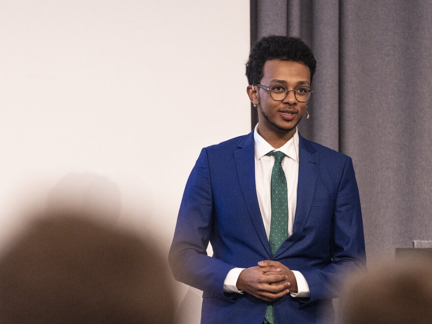 Mørkhudet ung mann med briller og blå dress holder foredrag