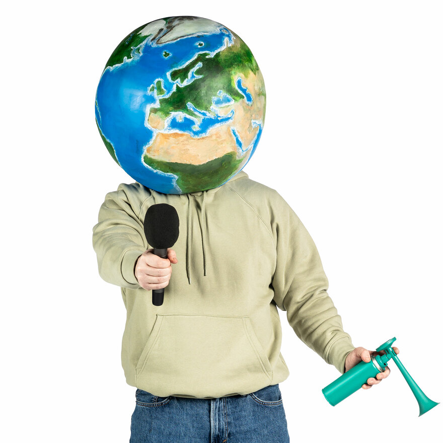 En person med en klode til hode, holder en mikrofon og et lufthorn.