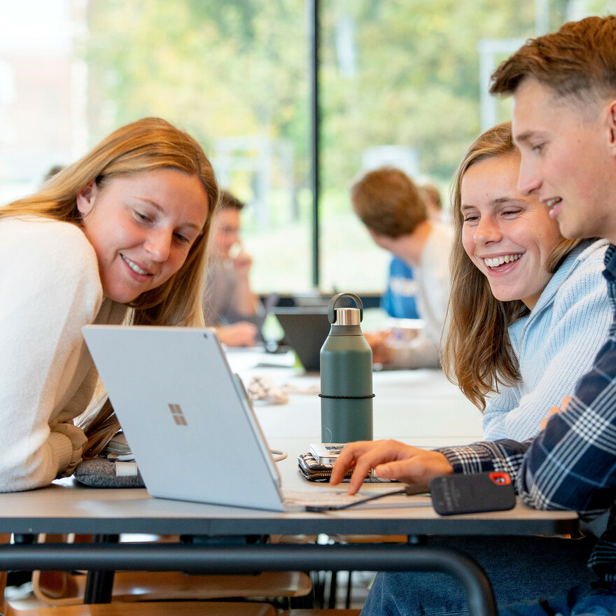 To kvinnelige og en mannlig student ser på en laptop sammen