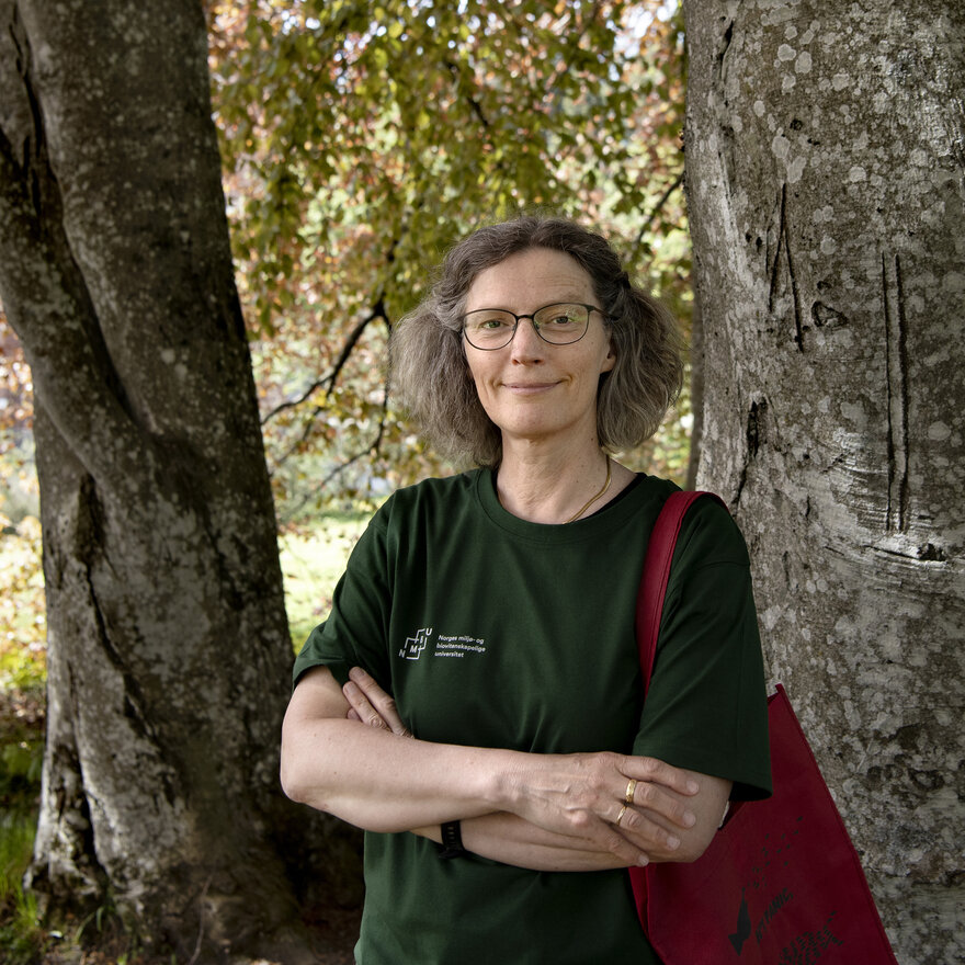 Anne Sverdrup-Thygeson utendørs foran to trær. 